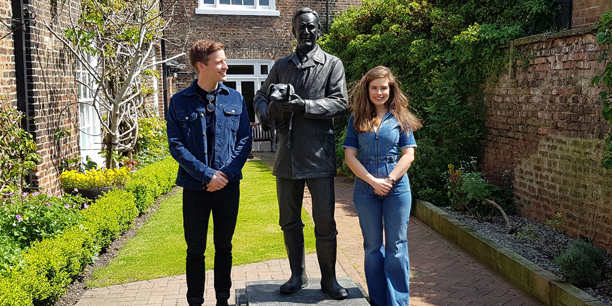 A man and a woman stand next to a statue of vet james Alfred Wight at The World of James Herriot