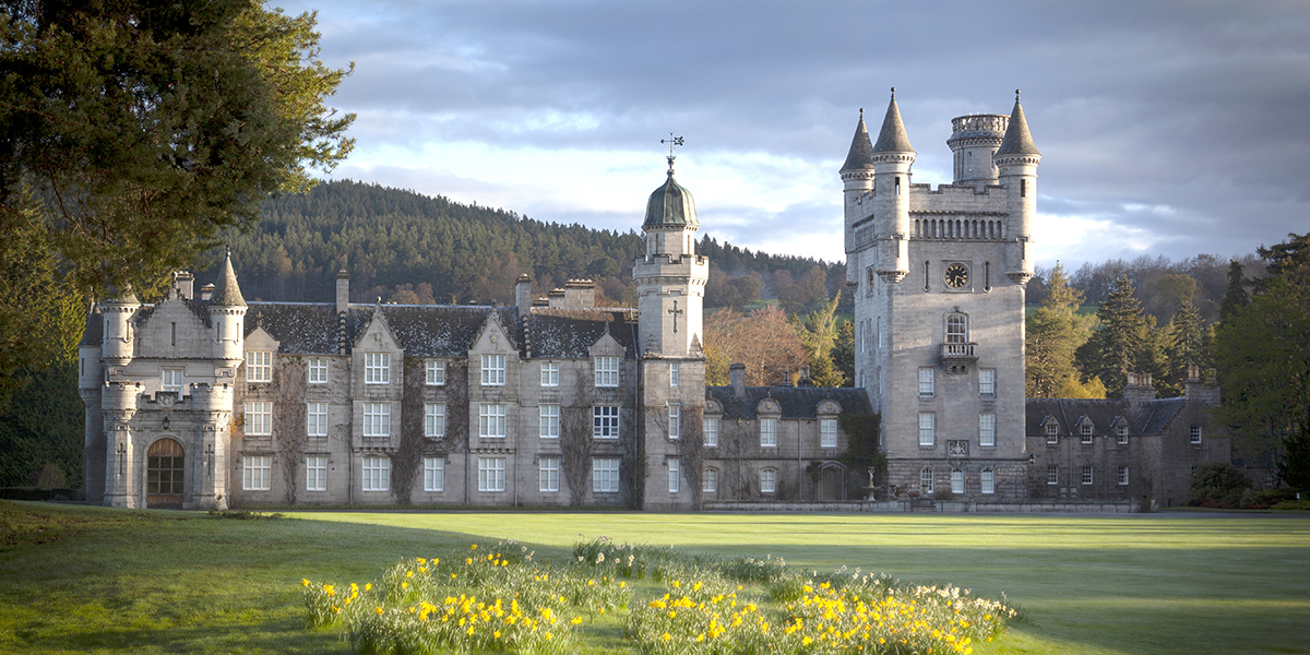 Picture of Balmoral Castle, with a scenic grassy field and trees surrounding the structure